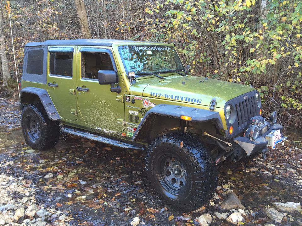 Green Jeep Wrangler with off-road mods driving through a stream.