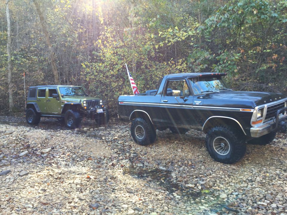 Black Ford Bronco and green Jeep Wrangler parked on a rocky stream bed.