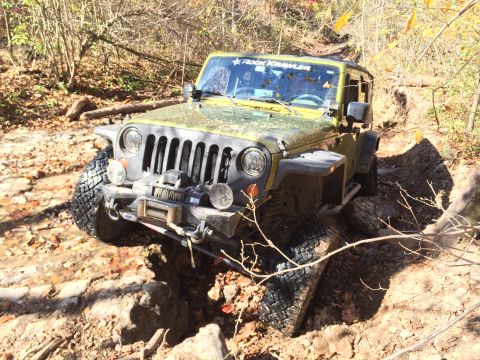 1979 Ford Bronco - A green Jeep Wrangler is navigating a rocky, off-road trail in a wooded area during autumn. The vehicle is angled towards the viewer, with…
