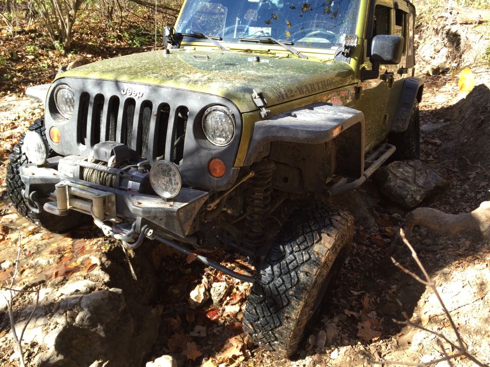Olive green Jeep Wrangler with winch and off-road tires on a rocky trail.