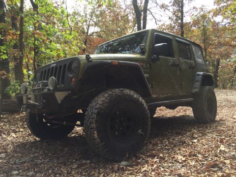 1979 Ford Bronco - A modified green Jeep Wrangler is parked on a dirt path covered in fallen leaves, surrounded by trees in autumn. The vehicle features large…