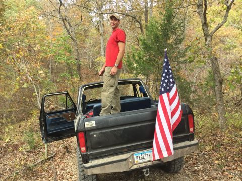 1979 Ford Bronco - A man in a red shirt and tan cargo pants stands in the bed of a black pickup truck, which has an American flag attached to the tailgate. Th…