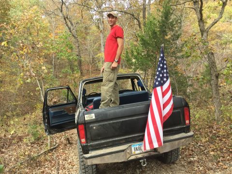 1979 Ford Bronco - A man stands in the bed of a black Ford pickup truck with the driver's side door open, an American flag attached to the tailgate, and an of…