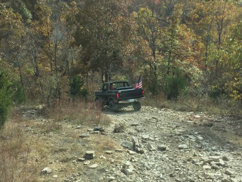 1979 Ford Bronco - A black 1979 Ford Bronco with an American flag in the bed is parked on a rocky, wooded trail during the fall.