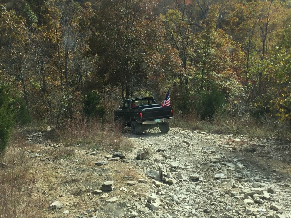 Black 1970s Ford pickup truck with American flag on a rocky trail.