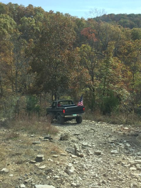 1979 Ford Bronco - A black Ford pickup truck with an American flag in the bed is parked on a rocky, wooded trail during the fall.