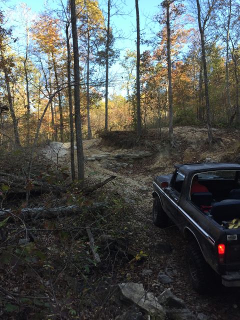1979 Ford Bronco - A red convertible sits parked on a dirt road surrounded by trees in autumn foliage.