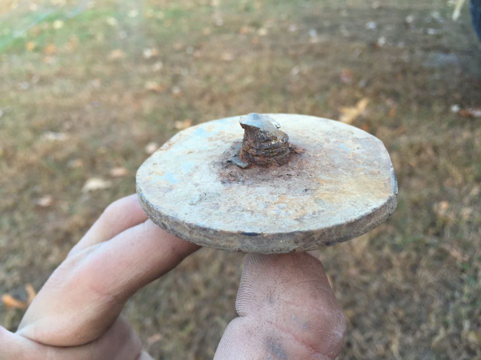 Close-up of a rusty metal disc with a bolt, held by fingers.