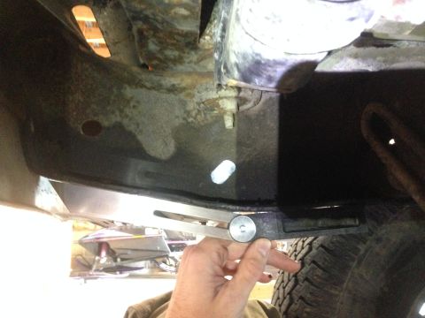 1979 Ford Bronco - A close-up view of a person's hand holding a bolt near the underside of a vehicle's frame. A metal plate is being installed or removed, wit…