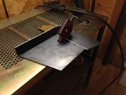 1979 Ford Bronco - A metal fabrication project is underway on a workbench. A piece of bent sheet metal is positioned on a metal grate, with a red magnetic wel…