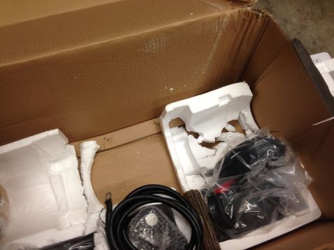 1979 Ford Bronco - An open cardboard box containing packing material and a black object wrapped in plastic, possibly a vehicle part. A coiled black cable is a…