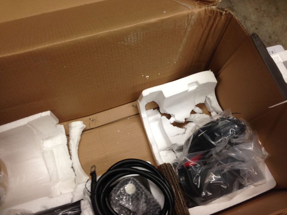 Open box with packing material and a wrapped black object.