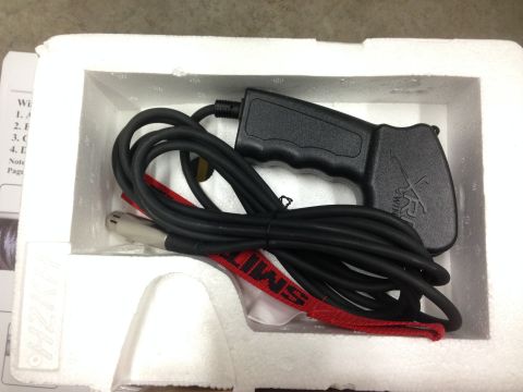 1979 Ford Bronco - A black winch remote control with a coiled black cable and a silver connector is nestled in white styrofoam packaging. A red strap with bla…