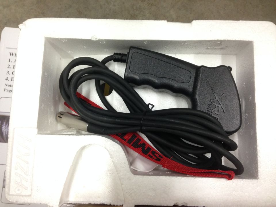 Black winch remote control with coiled cable and red strap in white styrofoam packaging.