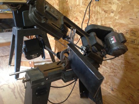 1979 Ford Bronco - A metal cutting bandsaw is shown in a workshop setting. The saw is on a stand with a motor attached.