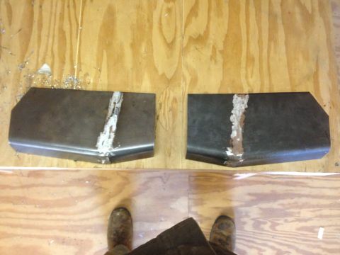 1979 Ford Bronco - Two custom metal brackets with white residue are laid out on a plywood surface. Metal shavings are visible to the left of the bracket on th…