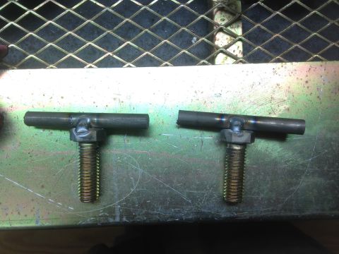 1979 Ford Bronco - Two T-shaped metal pieces are welded onto bolts. They are resting on a metallic surface.