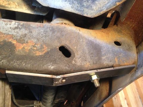 1979 Ford Bronco - A close-up view of a rusty, modified vehicle frame with a newly added metal plate bolted to the underside. The metal plate appears to be a…