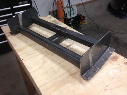 1979 Ford Bronco - A custom-fabricated metal frame rests on a wooden workbench. The frame appears to be constructed from square steel tubing and flat steel pl…