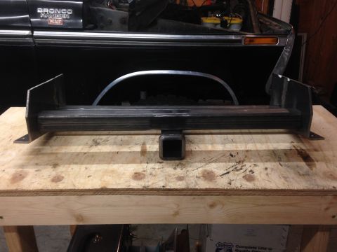 1979 Ford Bronco - A custom-fabricated steel trailer hitch receiver assembly is displayed on a wooden workbench in front of a black 1979 Ford Bronco.