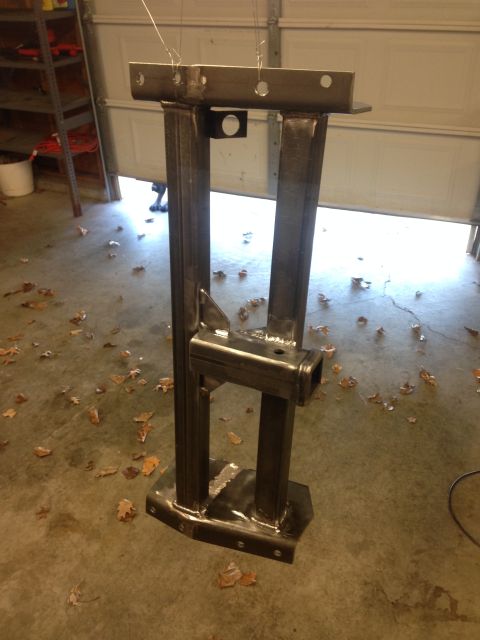 1979 Ford Bronco - A custom-fabricated steel trailer hitch receiver is suspended by wires in a garage, ready for finishing. The hitch features a square receiv…