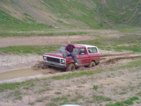 1978 Ford Bronco - Man sits on the hood of a red 1978 Ford Bronco as it gets stuck in the mud.