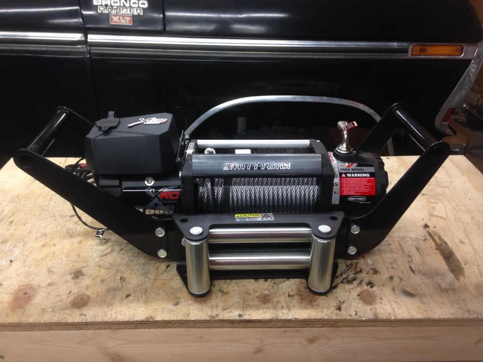 Smittybilt XRC winch mounted on a black frame, in front of a black vintage vehicle.