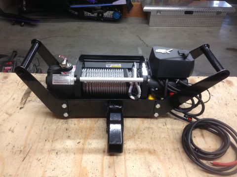 1979 Ford Bronco - A black electric winch mounted on a black metal frame with a hitch receiver is displayed on a wooden surface. The winch has a steel cable w…