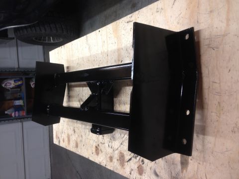 1979 Ford Bronco - A black metal trailer hitch receiver is mounted on a wooden surface, likely in a garage. The receiver has a horizontal bar with two vertica…