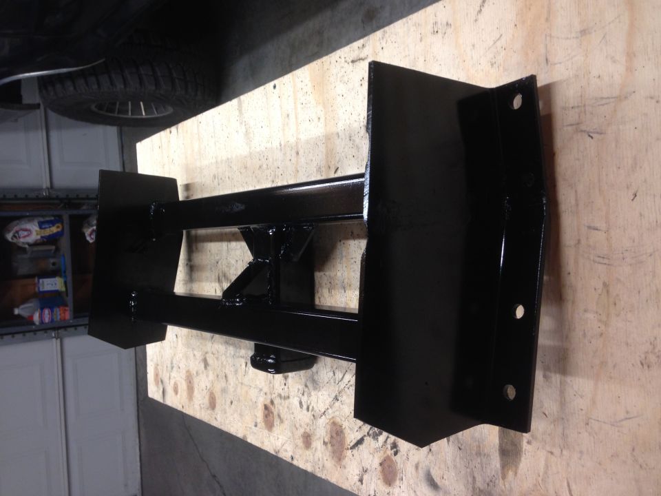 Black trailer hitch receiver with mounting plates and bolt holes on a wooden surface.