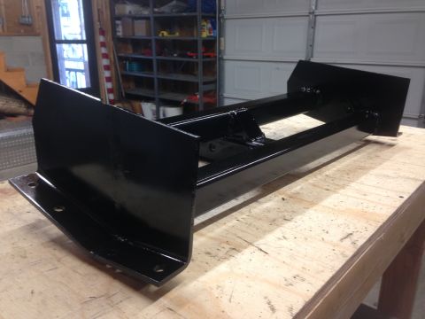 1979 Ford Bronco - A black metal plow attachment with mounting brackets is displayed on a wooden workbench in a garage setting. The attachment appears to be c…