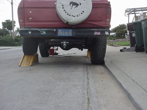 1978 Ford Bronco - The rear of a red Ford Bronco is elevated on yellow ramps for maintenance, with a spare tire mounted on the tailgate.