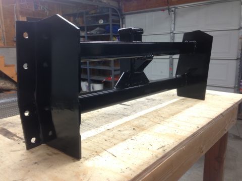 1979 Ford Bronco - A black metal fabrication, possibly a hitch receiver or mounting bracket, is shown resting on a wooden workbench in a garage setting. The p…