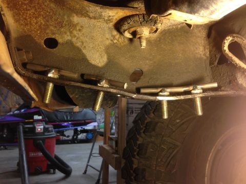 1979 Ford Bronco - Custom metal brackets with bolts are installed onto the rusty frame of a vehicle, positioned above a tire. The scene appears to be in a gar…