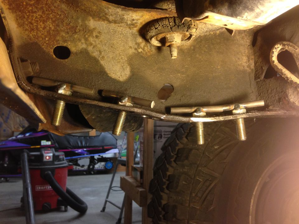 Custom metal brackets bolted to a rusty vehicle frame above a tire.