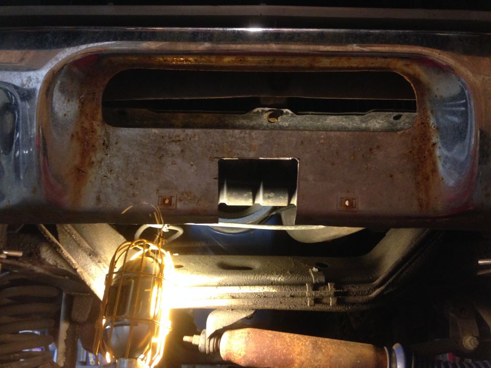 Close-up of rusted front bumper and underside of a vintage vehicle with a work light.