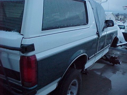 1996 Ford Bronco - This two-tone SUV is partially covered by a tarp, showing its side profile and rear taillight.