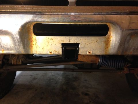 1979 Ford Bronco - The front of a vehicle shows a chrome bumper with a hitch receiver and signs of rust.