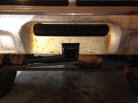 1979 Ford Bronco - Close-up of a trailer hitch receiver mounted on a heavily rusted bumper, showing mechanical parts underneath.