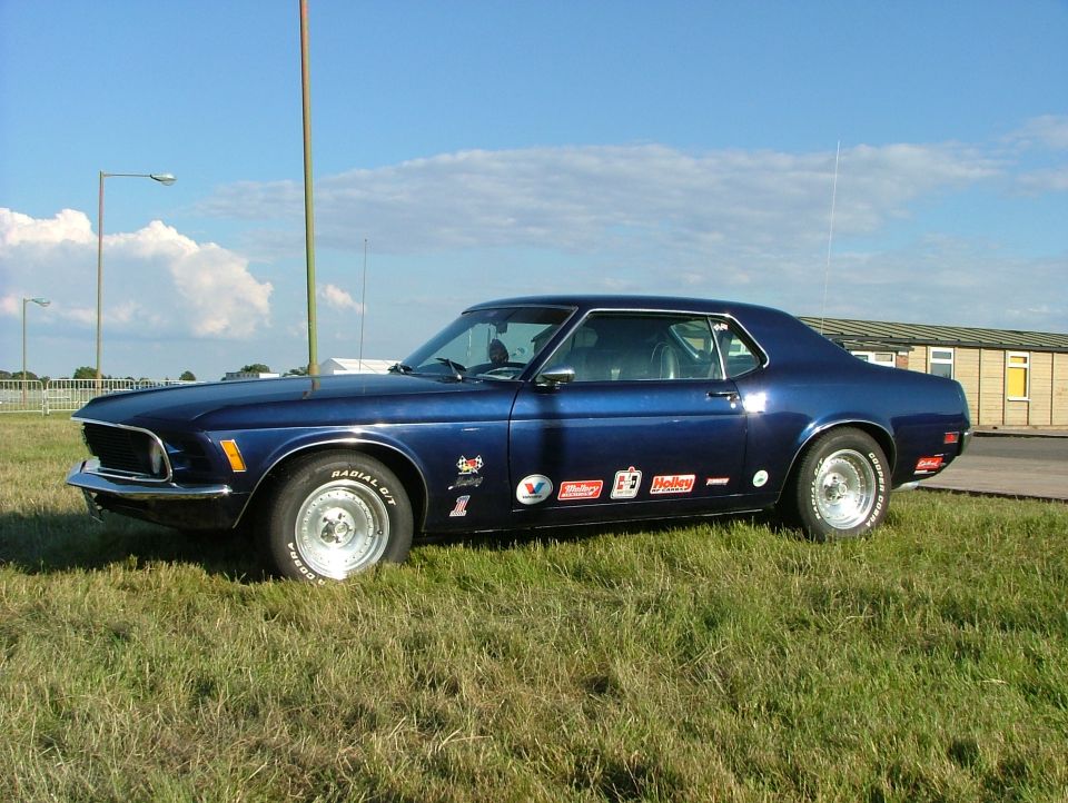Blue 1970 Ford Mustang coupe with racing decals on the side, parked on grass