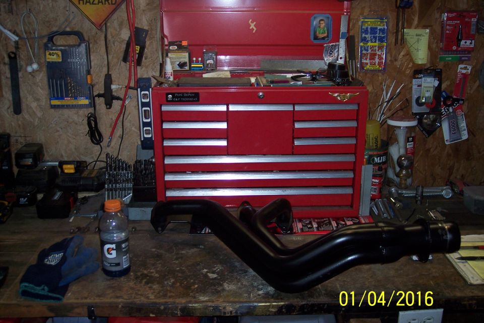 Black exhaust manifold on a workbench with a red toolbox and Gatorade bottle.