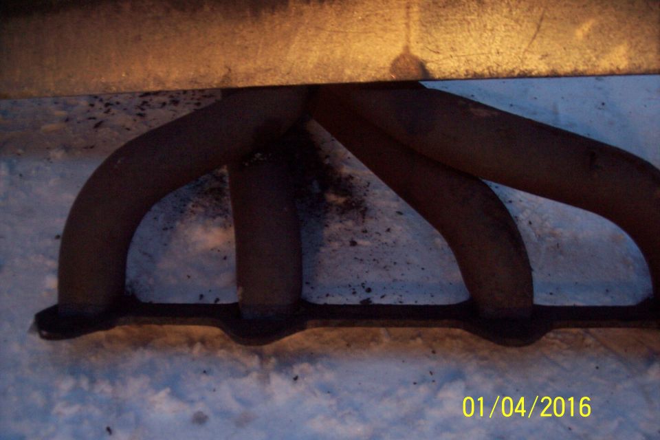 Rusty exhaust manifold with four pipes on a snowy surface.