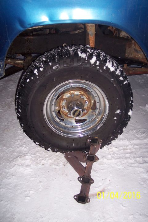 1973 Ford F-250 - A close-up view of a snow-covered tire and rim on a blue vehicle, with a rusty exhaust manifold lying in the snow underneath. A date stamp…