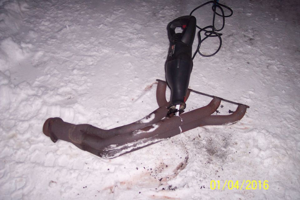 Reciprocating saw cutting a rusty exhaust manifold in the snow.