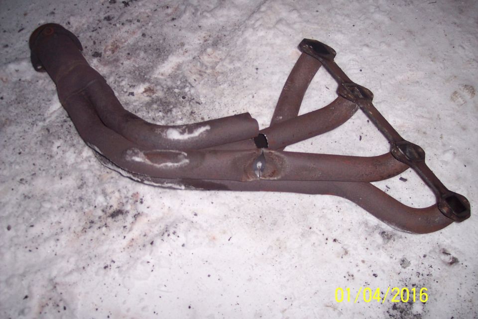 Rusty exhaust manifold with four pipes, one broken and welded, on a snowy surface.