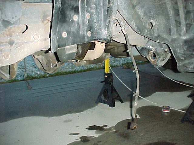 Close-up of vehicle frame and suspension parts supported by jack stands. Brake line visible