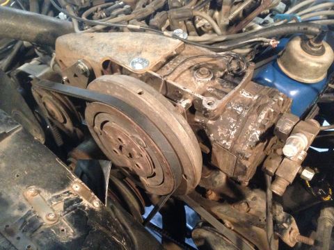1979 Ford Bronco - A close-up view of the engine bay of a 1979 Ford Bronco, focusing on the air conditioning compressor and serpentine belt system. The engine…