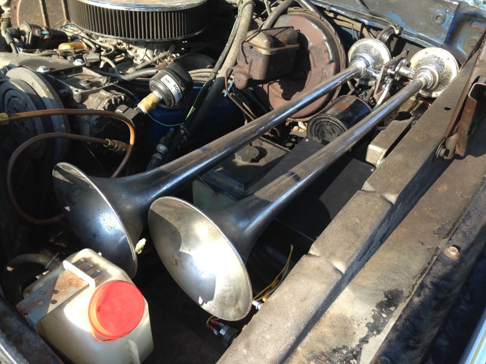 Dual trumpet air horns in the engine bay of a classic vehicle.