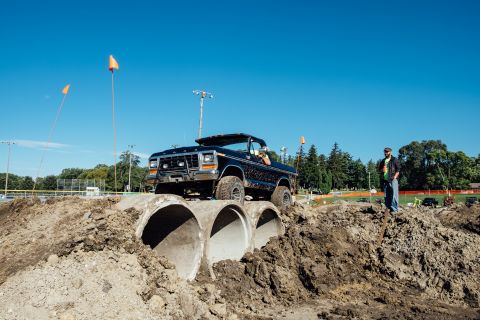 1979 Ford Bronco - A black Ford Bronco is driving over a series of large concrete pipes on a dirt track. A man in a black jacket and jeans stands on a mound o…