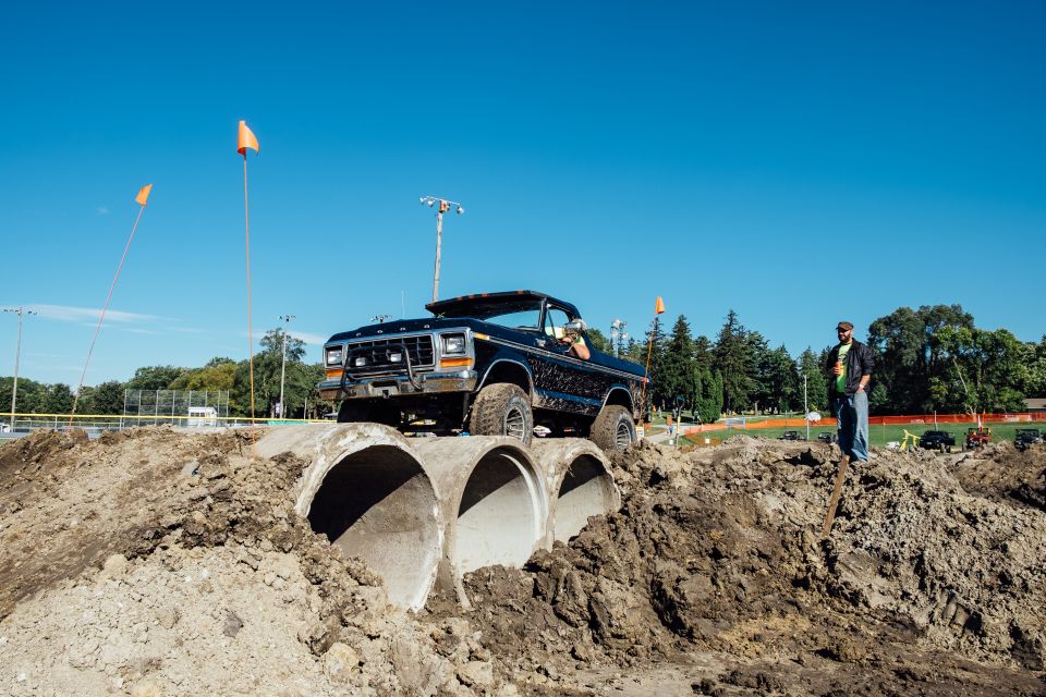 Black Ford Bronco driving over concrete pipes on a dirt track with a man watching.